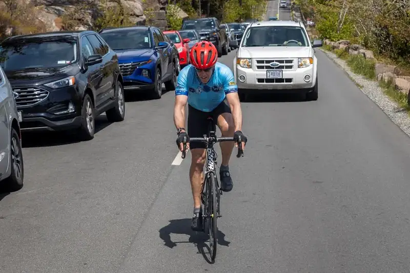 A cyclist rides down the middle of a congested Park Loop Road, surrounded by parked cars lining the road