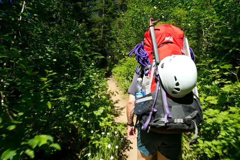 Person with backpacking and climbing gear hikes on a trail. 
