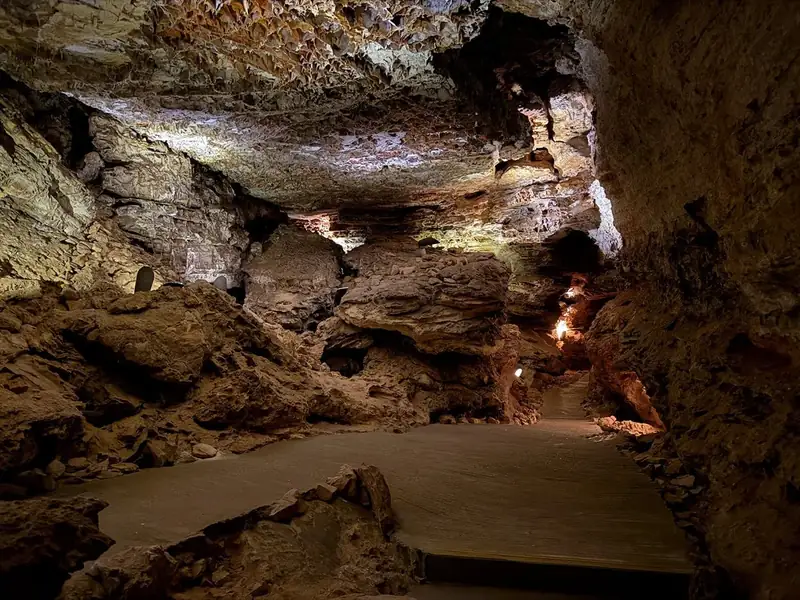 View of a cave room with yellowish-brown rocks and a criss-cross pattern of boxwork on the ceiling.