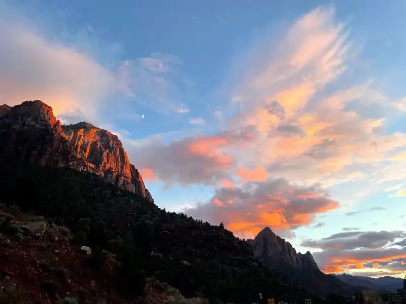 A crescent moon and pink clouds rest above a cliff illuminated by red light.