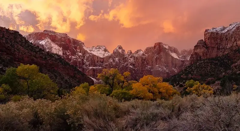 Clouds glowing pink, over red cliffs dusted with snow.